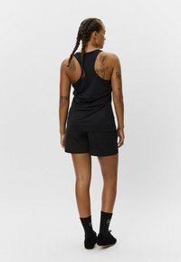 Čierny športový top s pretekárskym strihom, doplnený čiernymi šortkami. Nosené s čiernymi ponožkami a topánkami. Tetovania viditeľné na chrbte.