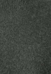 Tissu en laine gris foncé avec une texture douce et duveteuse, des fibres visibles dispersées sur la surface.