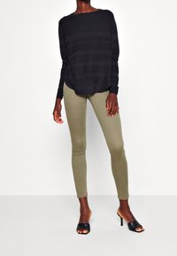 Haut à manches longues rayé noir associé à un pantalon skinny vert olive. Les chaussures sont des mules à talons noires ouvertes à l'avant.