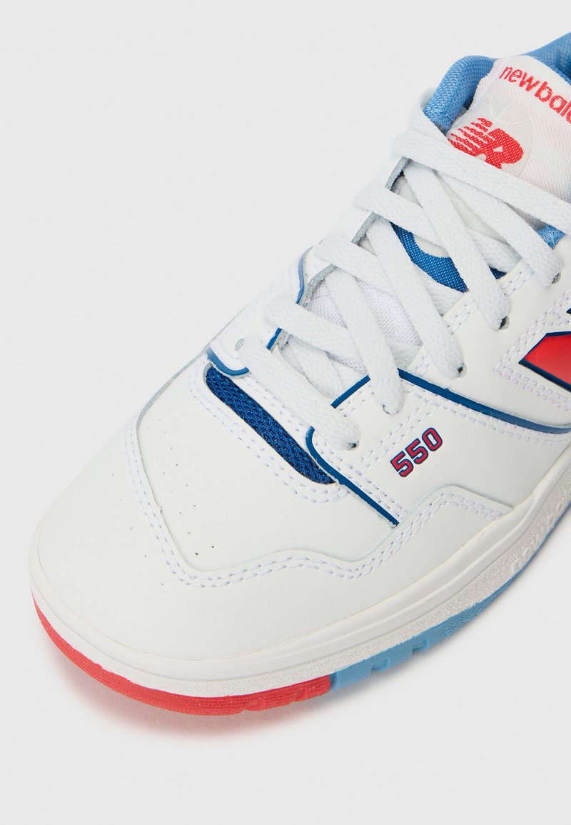 Sneaker New Balance 550 bianco con dettagli rossi e blu, lacci bianchi e "550" stampato sul lato vicino alla punta.