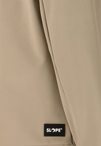 Tissu beige avec une texture lisse, présentant une petite étiquette noire SLOPE®. Le design inclut un léger gaufrage pour plus de détails.