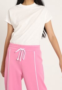 Camiseta de algodón blanca de manga corta combinada con pantalones de chándal rosa con cordón blanco y detalles de piping en los laterales.