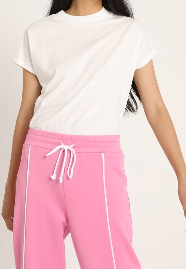 Camiseta de algodón blanca de manga corta combinada con pantalones de chándal rosa con cordón blanco y detalles de piping en los laterales.