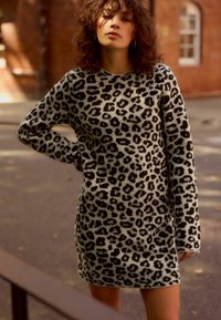 Abito lavorato a maglia con motivo leopardato, maniche lunghe, scollatura rotonda e vestibilità comoda. Il tessuto è morbido, con uno sfondo beige chiaro e macchie scure.