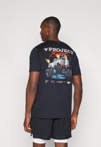 Black cotton t-shirt with graphic print featuring a monster truck, flames, and logos. Short sleeves, round neck, relaxed fit.