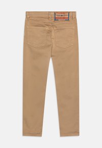 Pantalones de mezclilla en tono beige con corte slim. Presentan bolsillos traseros con un patrón de costura sutil y una etiqueta de la marca en la cintura. Textura suave.