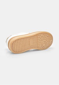 Sneaker sole with textured rubber in beige, featuring triangular patterns and circular accents. White upper partially visible at the edge.
