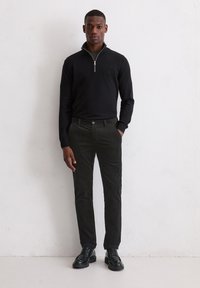 Pull noir à col zippé, pantalon en velours côtelé gris slim-fit, et chaussures à lacets noires. Texture lisse et design minimaliste sans motifs.