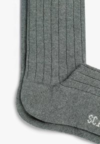 Calcetines gris con textura acanalada suave, tejido plano y talón reforzado. Incluyen una etiqueta blanca de talla cerca del puño.