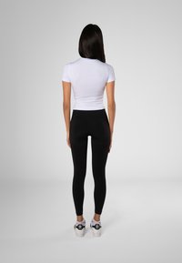 Hvit kortermet tettsittende topp kombinert med svarte høye leggings og hvite sneakers med svarte detaljer, sett fra baksiden.