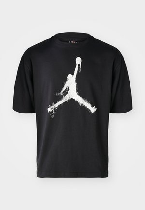 T-shirt en coton noir avec un grand motif en silhouette blanche représentant une figure en train de sauter, avec un ballon de basket centré sur la poitrine.