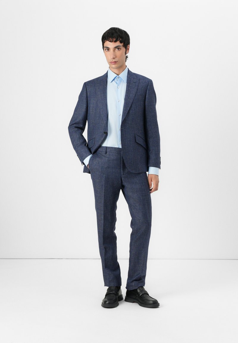Marineblauer maßgeschneiderter Anzug aus strukturiertem Stoff, bestehend aus einem Ein-Knopf-Blazer und passender Hose, kombiniert mit einem hellblauen Hemd und schwarzen Schuhen.