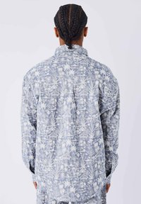 Lange mouwen shirt van lichtblauwe stof met wit tropisch patroon, voorzien van palmbomen en huizen, vrije pasvorm met een rugpas.