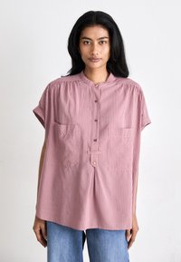 Ριγέ ροζ πουκάμισο με μαandarin κολάρο, κοντά αναδιπλωμένα μανίκια, δύο τσέπες στο στήθος και κουμπάκια μπροστά. Λείο υφασμάτινο υλικό.