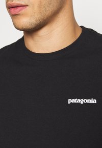 Fekete pamut póló, kerek nyakkivágással és egy kis fehér "Patagonia" logóval a bal mellrészen. Puha tapintású, minimalista dizájn.