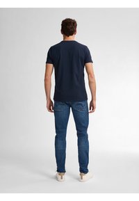 Marinblå T-shirt med rund hals i kombination med blå jeans. T-shirten har korta ärmar och en figurnära design. Skorna är vita med beige detaljer, i en avslappnad stil.