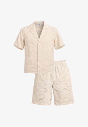 Camicia beige a maniche corte con bottoni e collo a risvolto abbinata a pantaloncini con vita elastica coordinati, adatta per un abbigliamento estivo casual.