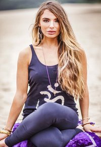 Svart ärmlös linne med silvergrafik, kombinerat med mörka leggings. Långt, vågigt hår och lager av smycken, sittande på en lila textil.