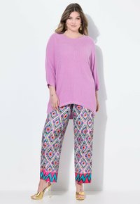 Luftiges, hellrosa Oberteil mit gerippter Textur, kombiniert mit gemusterten Hosen in lebhaften Farben. Goldene Akzentabsätze runden den Look ab.