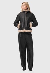 Svart skinnjacka med beige fårskinnsdetaljer, dragkedja och sidofickor; kombinerad med högmidjade svarta skinnbyxor.