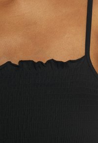 Haut en tissu côtelé noir avec des bretelles spaghetti réglables, présentant un bord froncé au niveau du décolleté et un design texturé ajusté.