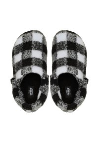 Pantofole in pile a quadri bianco e nero, con una texture morbida, forma arrotondata e design slip-on, dotate di un'etichetta con logo vicino al tallone.