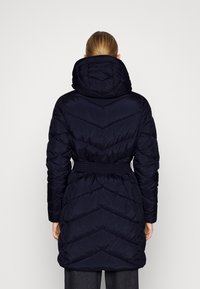 Tmavě modrý prošívaný kabát s kapucí, s páskem v pase a vzorem šipek. Vyrobený z hladké, lesklé látky.