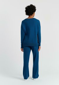 Blauwe gebreide trui met brede hals en lange mouwen, gecombineerd met bijpassende flared broek. Gecoate textuur en een ontspannen pasvorm overal.