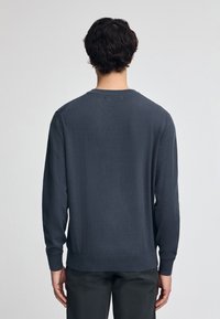 Pull en maille gris foncé avec des manches longues, encolure ras-du-cou et poignets côtelés. Texture lisse avec un léger éclat et une taille ajustée.