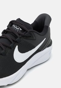 Zapatilla negra con parte superior de tejido texturizado, swoosh blanco de Nike y cuello acolchado. Presenta cordones negros y una suela de goma.