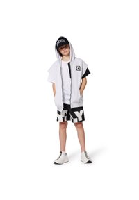 Haut sans manches gris avec un panneau noir, t-shirt blanc, shorts noirs avec de grandes lettres blanches, et baskets noir et blanc.