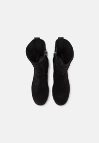 Paire de bottes mi-mollet en suède noir avec languettes de traction et boucles latérales, vues de dessus sur un fond blanc.