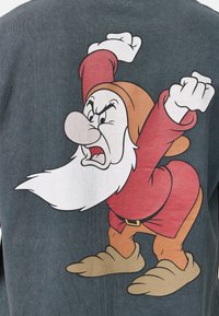 Camisa de manga larga gris con una gran ilustración colorida de un enano enojado con barba blanca, vestido con un traje rojo y zapatillas marrones.