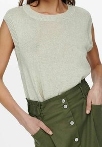 Hellgrünes gestricktes ärmelloses Oberteil mit rundem Halsausschnitt, kombiniert mit einem olivgrünen Rock mit hoher Taille, der silberne Knöpfe und seitliche Taschen hat.