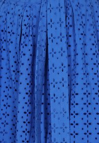 Tessuto blu con motivo ricamato a occhio di pernice floreale, caratterizzato da pieghe e finitura testurizzata. Misure e taglio non specificati.