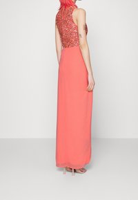 Abito maxi corallo con un corpetto di paillettes brillanti e design senza maniche, caratterizzato da una gonna fluente e un sovrapposto di tessuto trasparente.