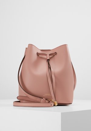 Sac seau en cuir rose doux avec fermeture à cordon et bandoulière ajustable sur une surface blanche.