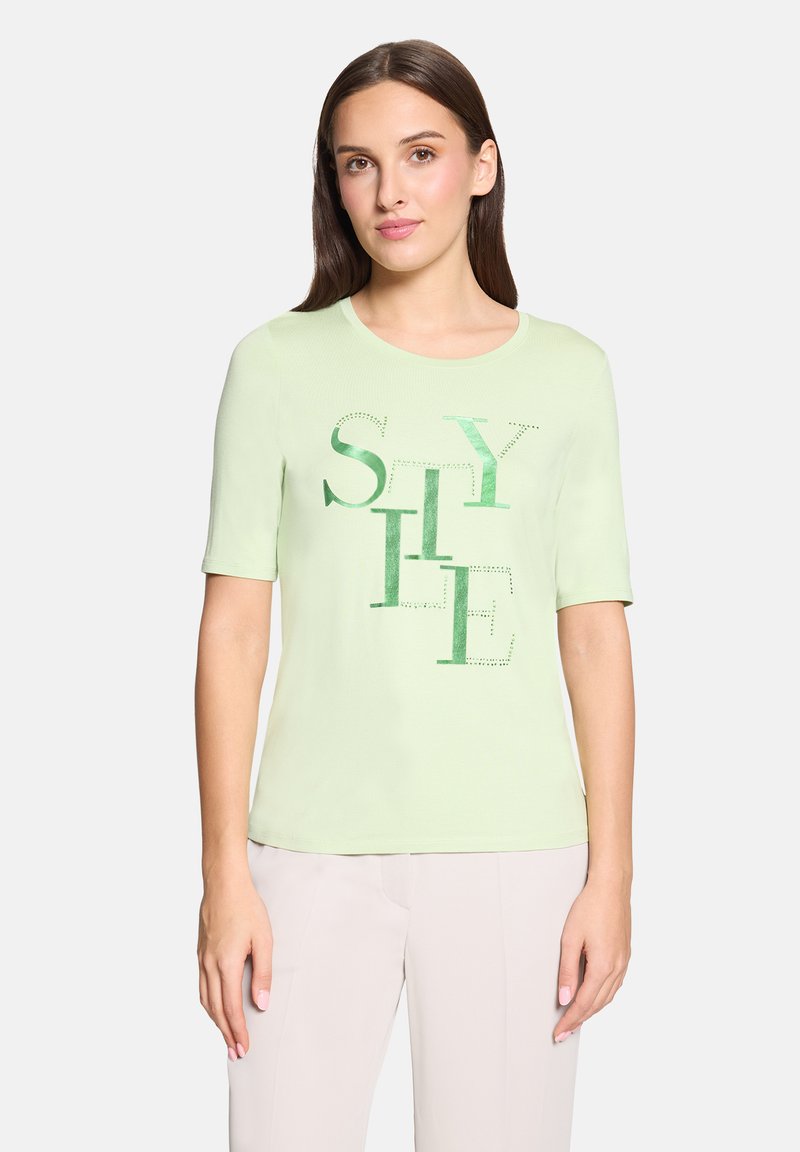 T-shirt à manches courtes vert clair avec le texte "STYLE" en différentes nuances et motifs verts, col rond, coupe ajustée et texture douce.