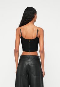 Μαύρο, εφαρμοστό cropped τοπ με φερμουάρ στην πλάτη, λεπτές ρυθμιζόμενες τιράντες και υφή υφάσματος. Συνδυασμένο με μαύρα δερμάτινα παντελόνια ψηλής μέσης.