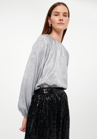 Silbernes Langarmtop mit gerafftem Ausschnitt und weicher Textur, kombiniert mit einem schwarzen, mit Pailletten besetzten Rock mit elastischem Bund.