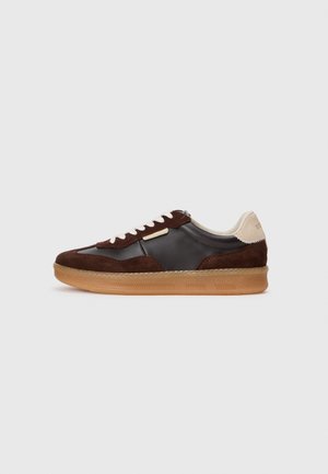 Brown suede and leather sneaker with a gum sole, featuring cream accents and white laces. Rounded toe and minimal detailing.