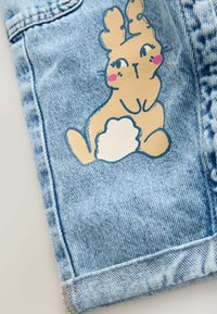 Denim szövet, világoskék színben. Díszítése egy bézs nyuszi minta, rózsaszín orcákkal és fehér farokkal, amely a ruhadarab alsó részén található.