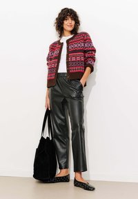 Gilet tricoté avec un motif multicolore de style fair isle, base marron ; associé à un pantalon en cuir synthétique noir et des ballerines noires à pois blancs.
