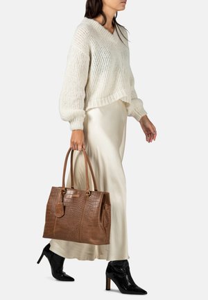Bruine tote bag met krokodillenstructuur, voorzien van dubbele handvatten, in combinatie met een crèmekleurige gebreide trui en een beige satijnen rok, aangevuld met zwarte haklaarzen.