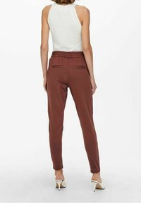 Brązowe dresowe spodenki z paskiem w talii, dwoma tylnymi kieszeniami i zwężanym krojem, zestawione z białą bluzką bez rękawów i butami na obcasie.