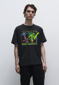 Černé bavlněné tričko s barevným grafickým logem MTV, které zobrazuje planety a neonové akcenty. Krátké rukávy a volný střih.
