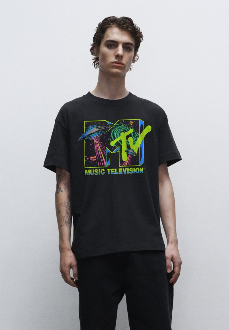Černé bavlněné tričko s barevným grafickým logem MTV, které zobrazuje planety a neonové akcenty. Krátké rukávy a volný střih.