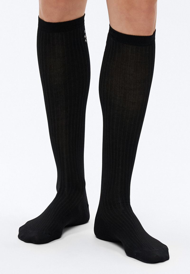 Põlveni ulatuvad mustad sokid vertikaalse soonikuga, millel on pehme tekstuur ja tihe istuvus, ülaservas tahke must mansett.