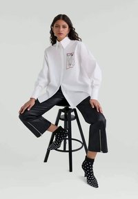 White button-up shirt with a graphic detail, paired with black leather pants featuring zippers, and black polka dot heeled ankle boots.