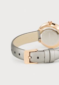 Orologio da donna con cassa rotonda in metallo rosa, dettaglio in cristallo trasparente e cinturino in pelle grigia chiara liscia con chiusura a fibbia.